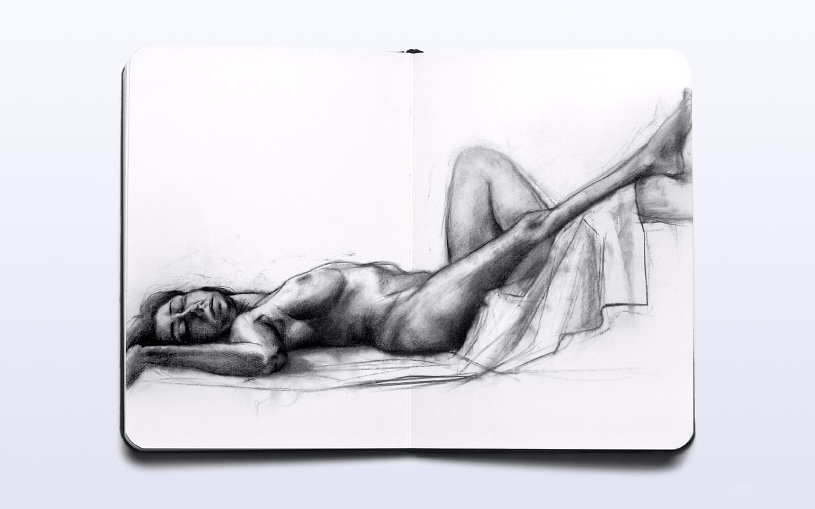 An open sketchbook featuring a nude woman lying on her stomach, highlighting the beauty of the human figure in art