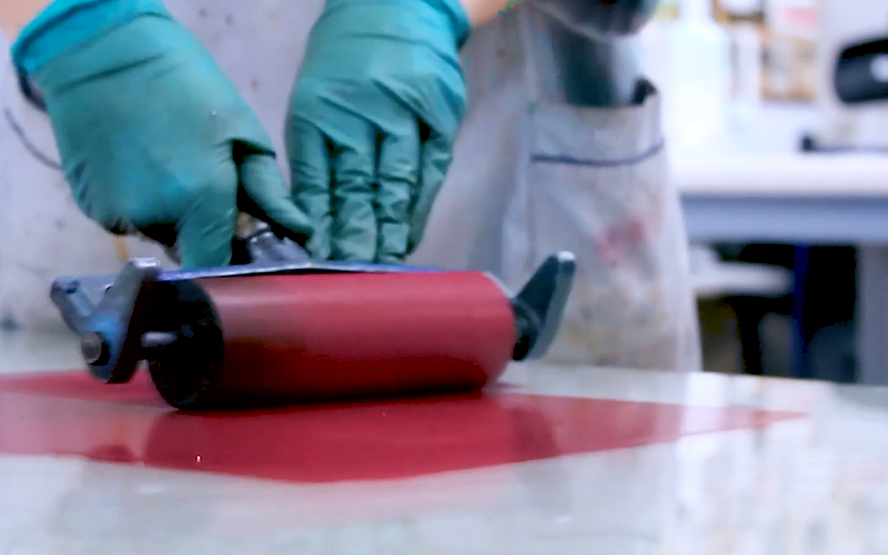 A person wearing a lab coat is holding a roller and red ink to print an engraving